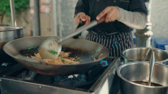泰国美食:女厨师在繁华的曼谷街头市场炒制美味的泰式炒粉