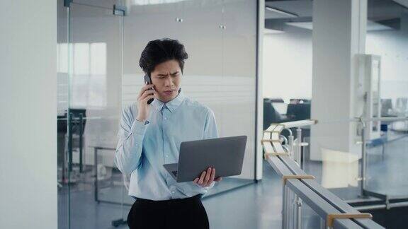 不满意的亚洲商人使用笔记本电脑在办公室打电话
