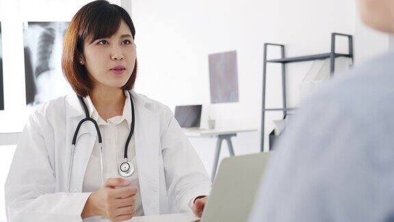 年轻的亚洲女医生正在用笔记本电脑传递好消息谈论结果或症状与男性病人坐在健康诊所的桌子上