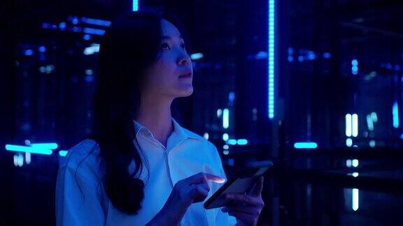 一名亚洲少女在夜晚使用5G移动智能手机在五颜六色的紫外线灯下观看移动互联网新一代网络可视化5g