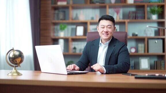 幸福的亚洲男性经理的肖像商人或会计律师公证人银行家在笔记本电脑上工作微笑看着相机坐在办公室的书桌