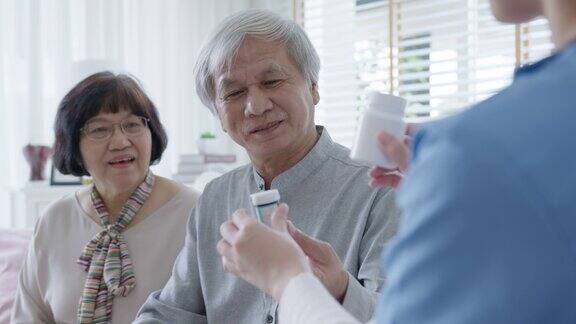 在家访护理服务中年轻的护理人员穿着手术服向年老的亚洲夫妇展示药瓶亚洲老年人与辅助生活药物监测概念