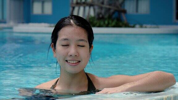 4K一个可爱的亚洲女游客是愉快地在游泳池游泳观光和放松的一天在酒店一个女人在一个晴朗的日子里一个人在游泳池里开心地游泳