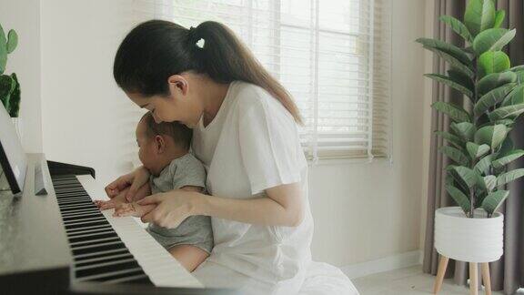 单亲妈妈抱着刚出生的小男孩的手在家里弹钢琴她教她可爱的孩子弹奏一种古典乐器