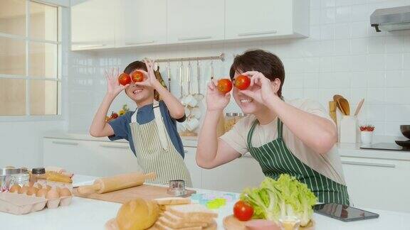 快乐微笑的年轻亚洲父子拿着西红柿在家里的厨房里享受烹饪