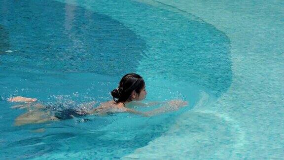 4K一个可爱的亚洲女游客是愉快地在游泳池游泳观光和放松的一天在酒店一个女人在一个晴朗的日子里一个人在游泳池里开心地游泳