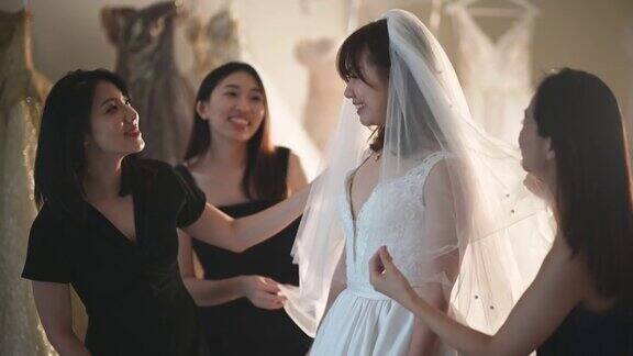 亚洲的中国新娘在婚纱店试穿婚纱伴娘在旁边欣赏婚纱的美丽