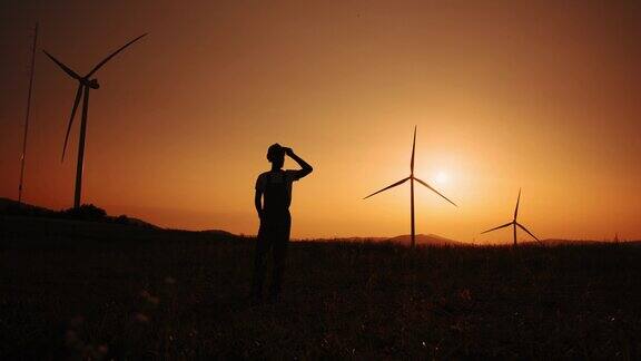 剪影非洲裔美国人站在场地上与巨大的风车在夏季日落环境污染替代能源的新技术风车的背景