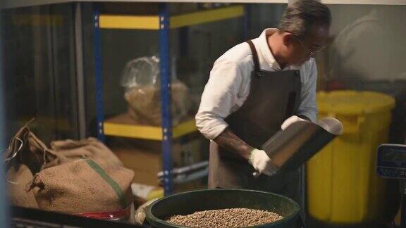 亚洲华人高级技工将生咖啡豆从桶中舀到秤机上并将其混合在工厂仓库的咖啡烘焙过程中