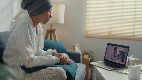 年轻的亚洲妇女生病的癌症使用笔记本电脑交谈医生坐在沙发上的客厅在家里