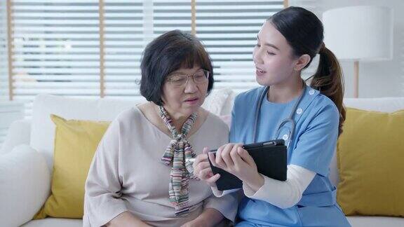 年轻的亚洲女性护士辅助生活家庭护理员或医生在家里拜访老年人在平板电脑上在线谈论结果跟踪检查表保健建议或处方
