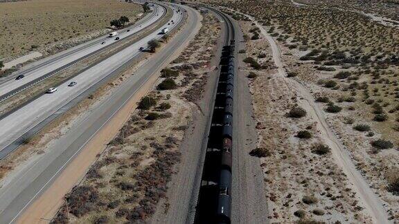 电影无人机拍摄飞行和下降到一个移动的货运列车与高速公路过往的汽车沙漠和更多在棕榈泉加州