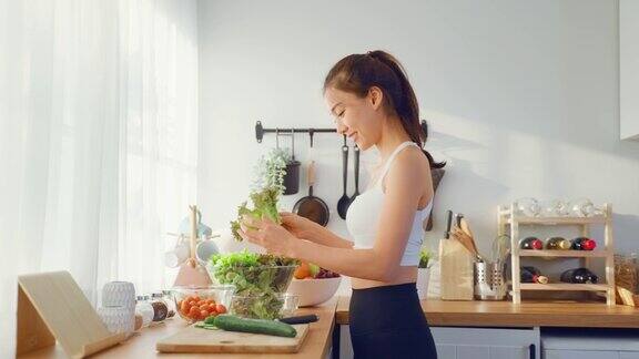 亚洲美女穿着运动服在厨房里做蔬菜沙拉年轻美丽的女孩感到快乐享受吃蔬菜健康的食物来减肥在家里的保健