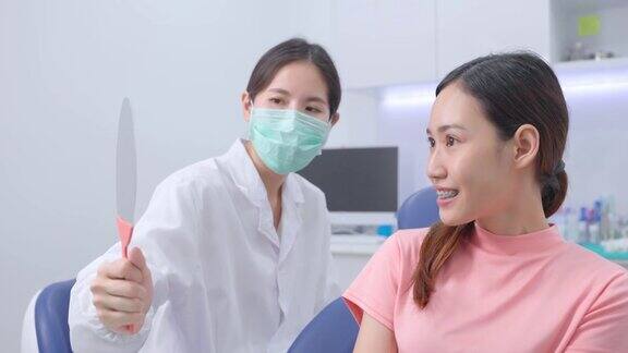 亚洲牙齿矫正医生拿着镜子让小女孩病人检查她的牙齿矫正女人看着镜子张大嘴巴看了看她的牙齿牙科诊所的口腔护理