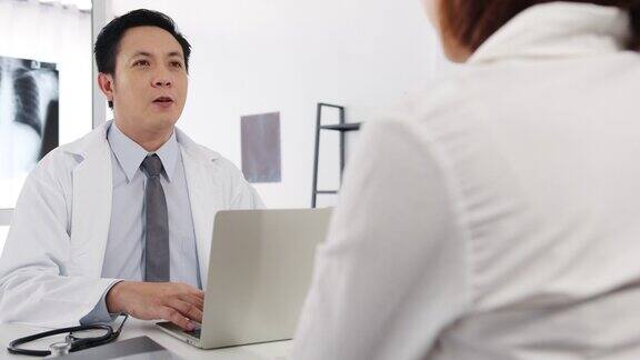 严肃的亚洲男医生正在用笔记本电脑传送好消息谈论结果或症状与女病人坐在医院办公室的桌子前