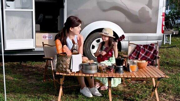 快乐的时刻一个亚洲小女孩在露营车自驾游的野餐桌上和她的母亲弹吉他
