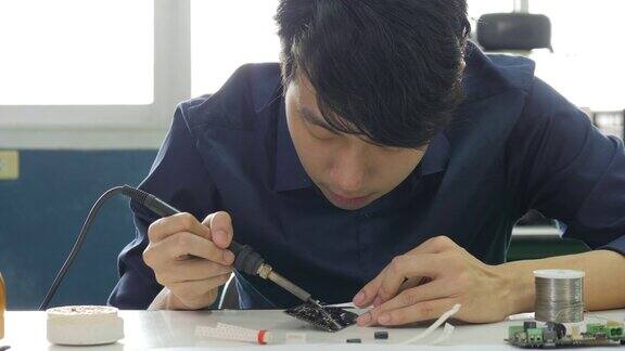 一位亚洲电子工程师正在他的车间里焊接一块电路板亚洲学生正在教室里学习电子学和焊接