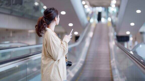 机场候机楼或现代火车站的年轻亚洲女性乘客亚洲女通勤者在自动扶梯上带行李