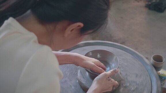 亚洲妇女粘土艺术家在她的工作室与纺纱陶轮工作