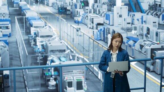 亚洲女工程师站在工厂设施里用笔记本电脑工作研究和开发现代自动化机械臂生产电子产品的技术