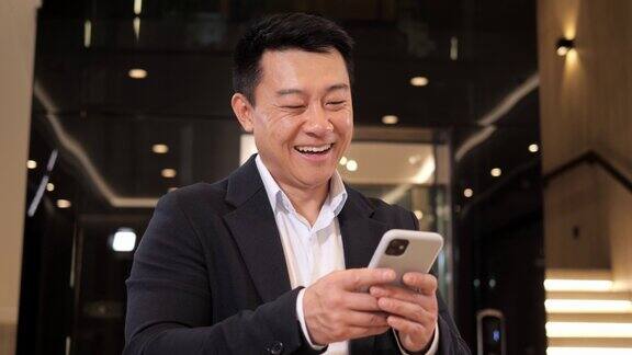 年轻英俊积极的商务男子手持智能手机设备发短信站在大厅办公室微笑使用移动应用程序在社交媒体聊天上网在室内电话