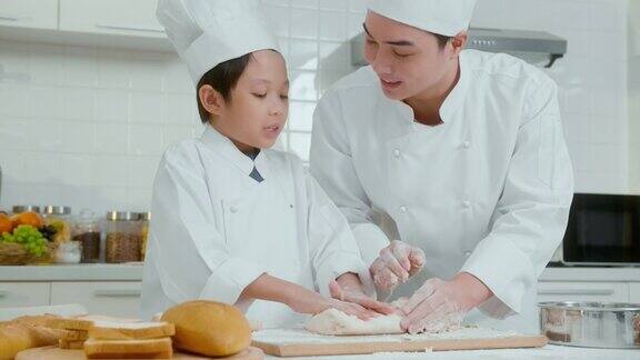 年轻的亚洲父亲和他的儿子穿着厨师制服在家里的厨房里一起烘焙