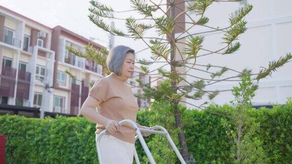 一位亚洲残疾老年妇女在绿色公园与行人一起慢步行走老年的成年病人残障女性下午在花园里进行物理治疗医疗保险