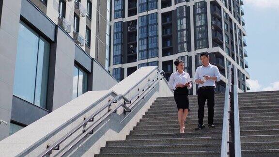 自信的跨国公司同事走下楼梯成功的亚洲华人商人和时髦的女人在街上交谈微笑的商务人士喝咖啡商务情侣休息