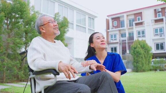 亚洲护理护士在户外照顾坐在轮椅上的老年男性美丽的专科女医生帮助和支持老年人成熟的老年病人男子在疗养院公园做物理治疗