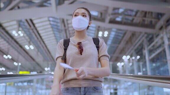 亚洲女性乘客在机场候机楼的自动扶梯上背着背包和行李箱旅行的正面照片新冠肺炎封锁结束后的旅行生活方式