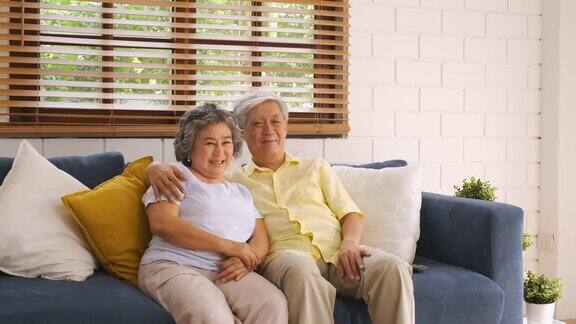 亚洲老夫妇坐在家里客厅的沙发上看电视从模糊前景电视平移