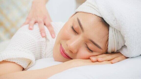 亚洲年轻女性感到快乐和放松在背部按摩油美丽迷人的女孩躺在按摩台上在spa美容院接受按摩师的皮肤和身体护理