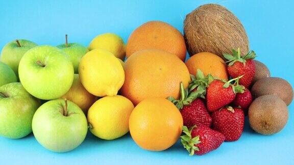 蓝色背景上的不同新鲜有机水果堆橘子苹果猕猴桃草莓柠檬和椰子