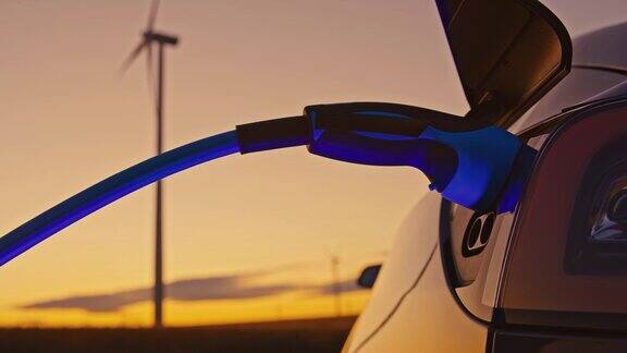 黄昏时分一个面目人非的女人在给自己的车插电动汽车插头她正在用风力涡轮机提供的蓝色能量为自己的电动汽车充电