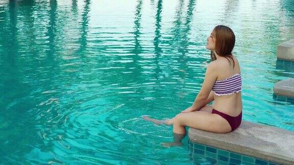 穿着泳装的年轻女子坐在游泳池边