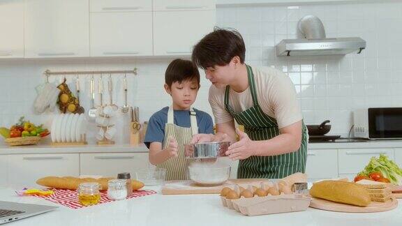 快乐的年轻亚洲父亲和儿子在家里的厨房里做饭