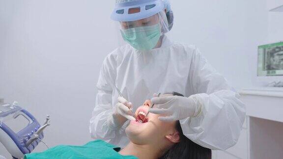 亚洲女牙医调整牙科手术灯然后开始检查或检查年轻女孩病人的牙齿躺在牙科椅上医生戴着防护口罩和防护罩进行卫生服务