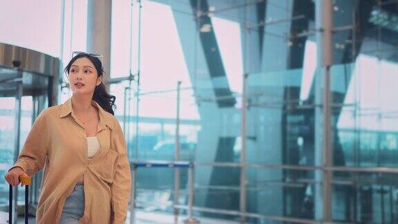 幸福微笑的亚洲女乘客带着行李箱走在机场候机楼