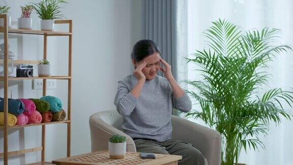 一位亚洲妇女坐在家里客厅的扶手椅上患了头痛