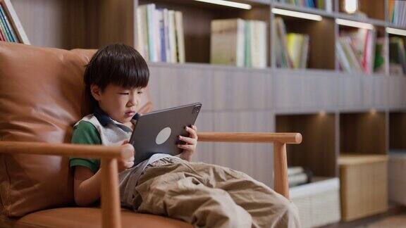 可爱的男生在家里拿着数码平板电脑进行在线学习