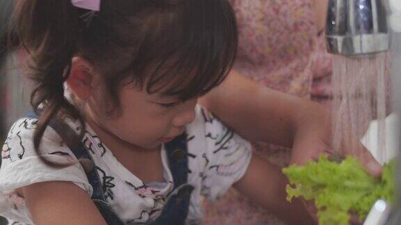亚洲母亲教她的女儿清洁和切片蔬菜在厨房家庭