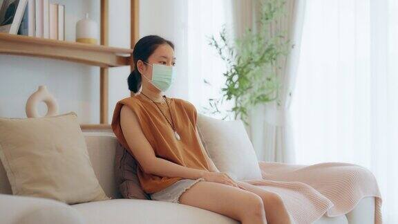 年轻的亚洲妇女坐在沙发上戴着口罩感冒发高烧保健和保险概念