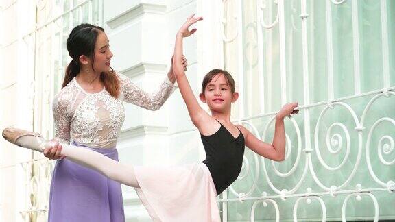 倾斜视图:一个晴朗的日子里一名亚洲青少年芭蕾舞演员在一名年轻女芭蕾舞老师的建议下在泰国曼谷当地的街道上练习芭蕾舞活跃的年轻妇女和孩子周末活动和当地地标