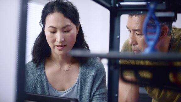 亚洲女工程师和她的亚洲男同事讨论建立一个双螺旋模型在3D打印机