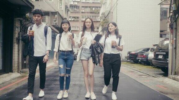 一群年轻的亚洲学生走在街上喝着珍珠奶茶(慢镜头)