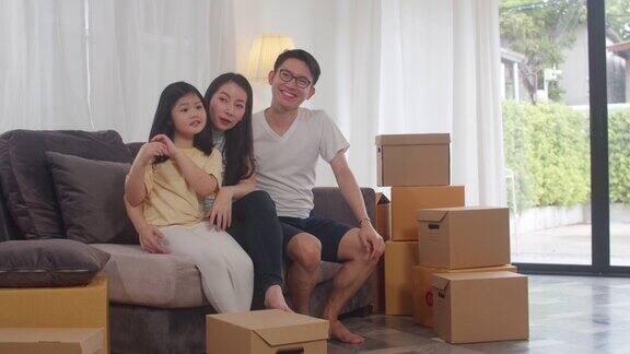 快乐的亚洲年轻家庭业主买了新房日本的妈妈爸爸和女儿拥抱期待未来在搬家后的新家与盒子一起坐在沙发上