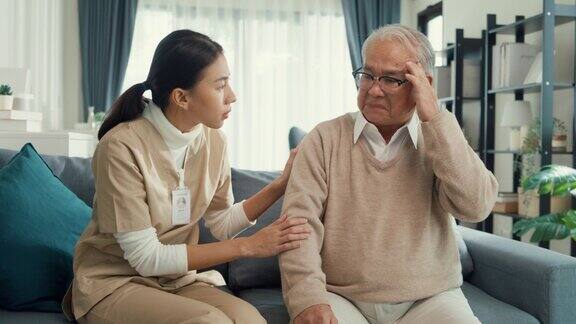 年轻的亚洲女性专业护理人员照顾触摸平静生病的老年男性病人在家里的客厅