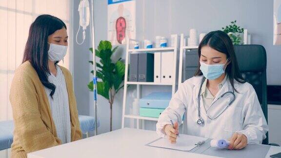 亚洲女性患者到年轻医生处就诊并咨询健康问题迷人的治疗师戴着口罩在办公室医院工作在大流行期间给生病的女孩治疗