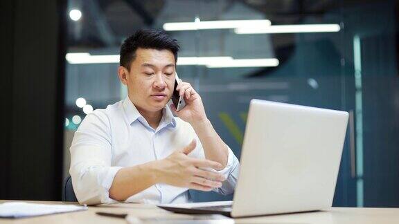 严肃的亚洲商人员工在笔记本电脑上工作在工作场所室内的现代办公室里打电话