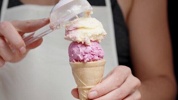 一个穿着白色围裙的女人用勺子把粉红色的冰淇淋球舀进华夫蛋筒里